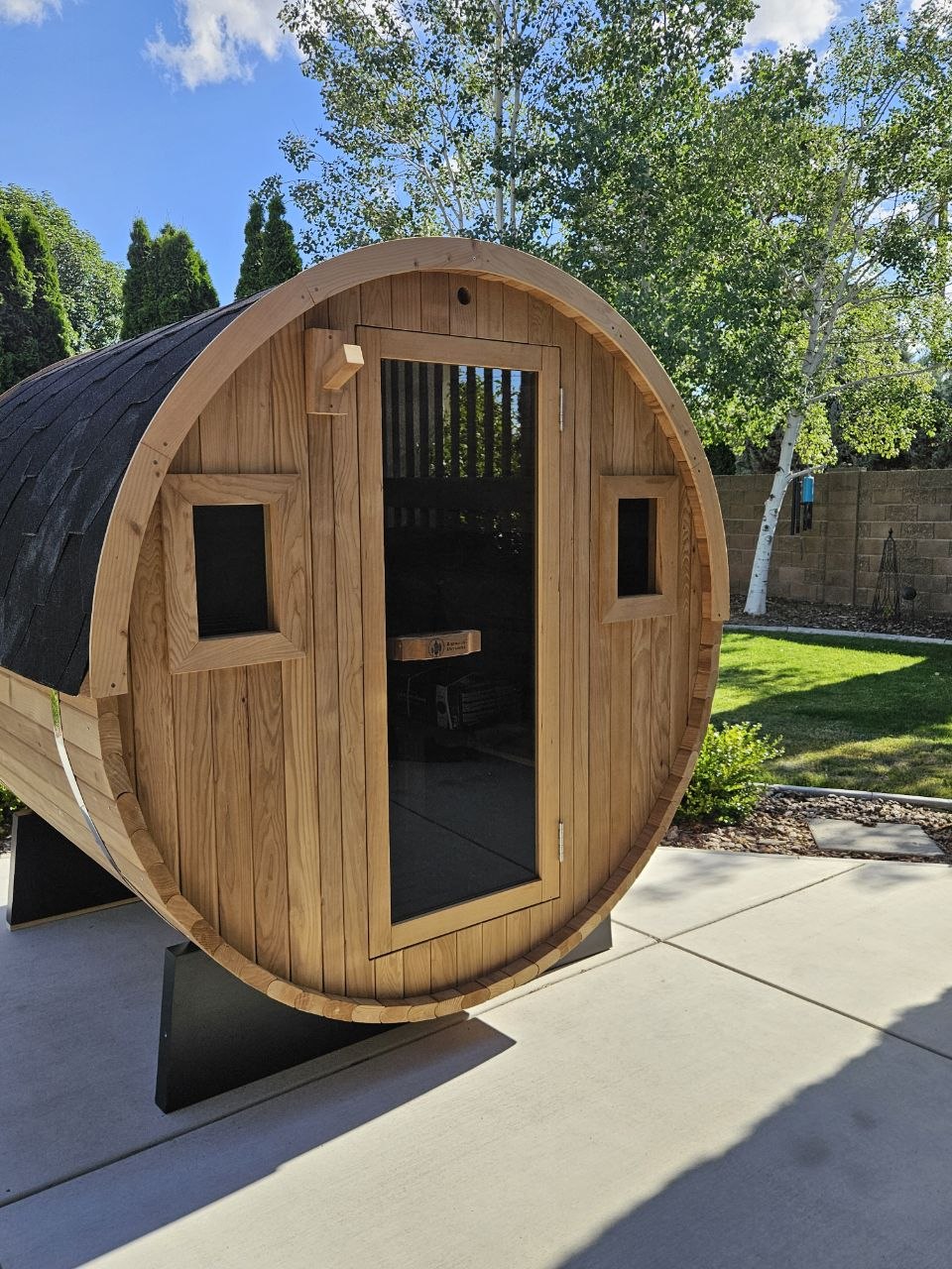 Redwood Outdoors barrel sauna with cedar construction and shingle roof delivered to landscaped backyard in Tri-Cities WA by AquaZen