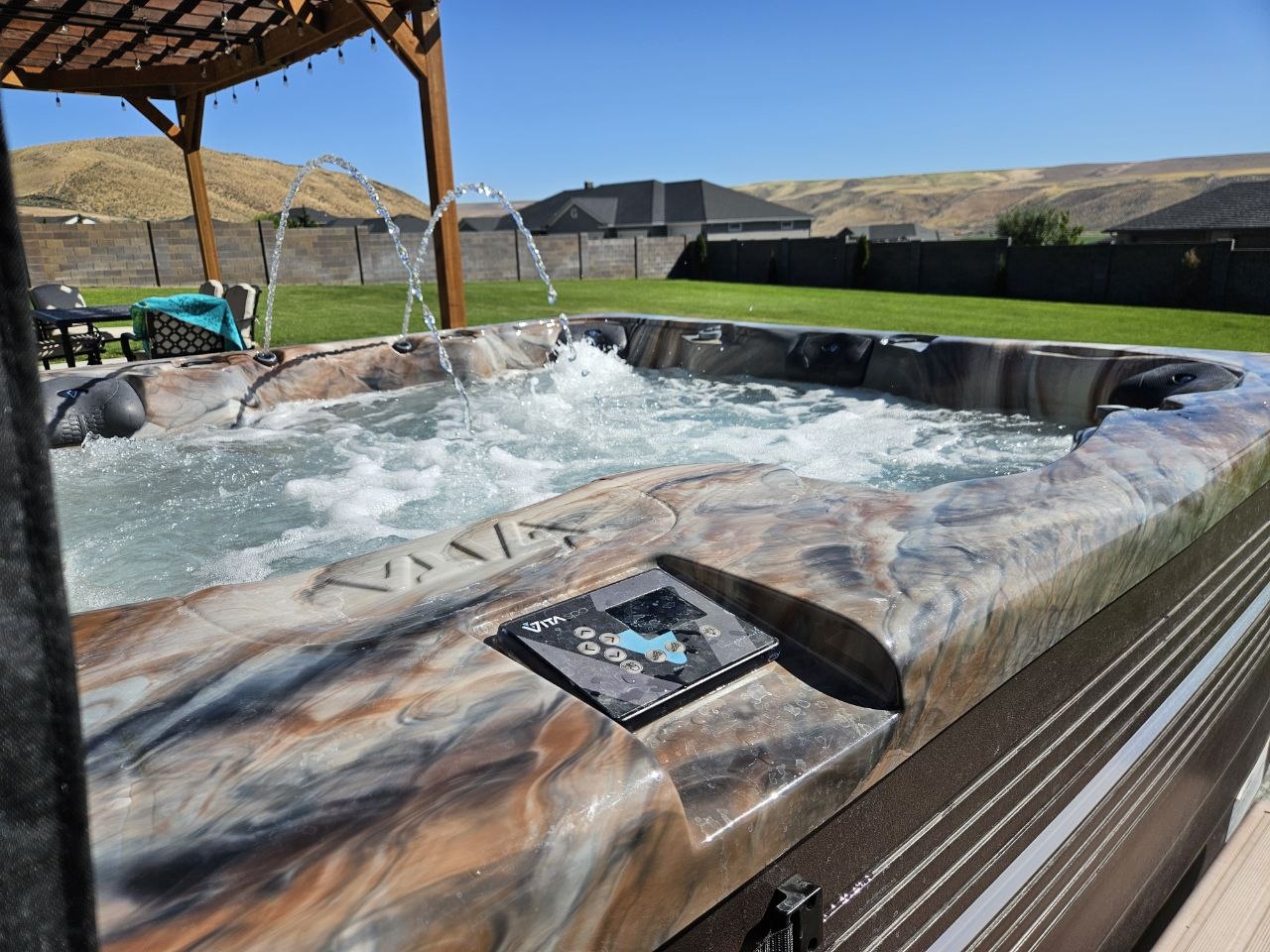 Vita Spa hot tub with water feature running under pergola with Tri-Cities hills in background — delivered by AquaZen