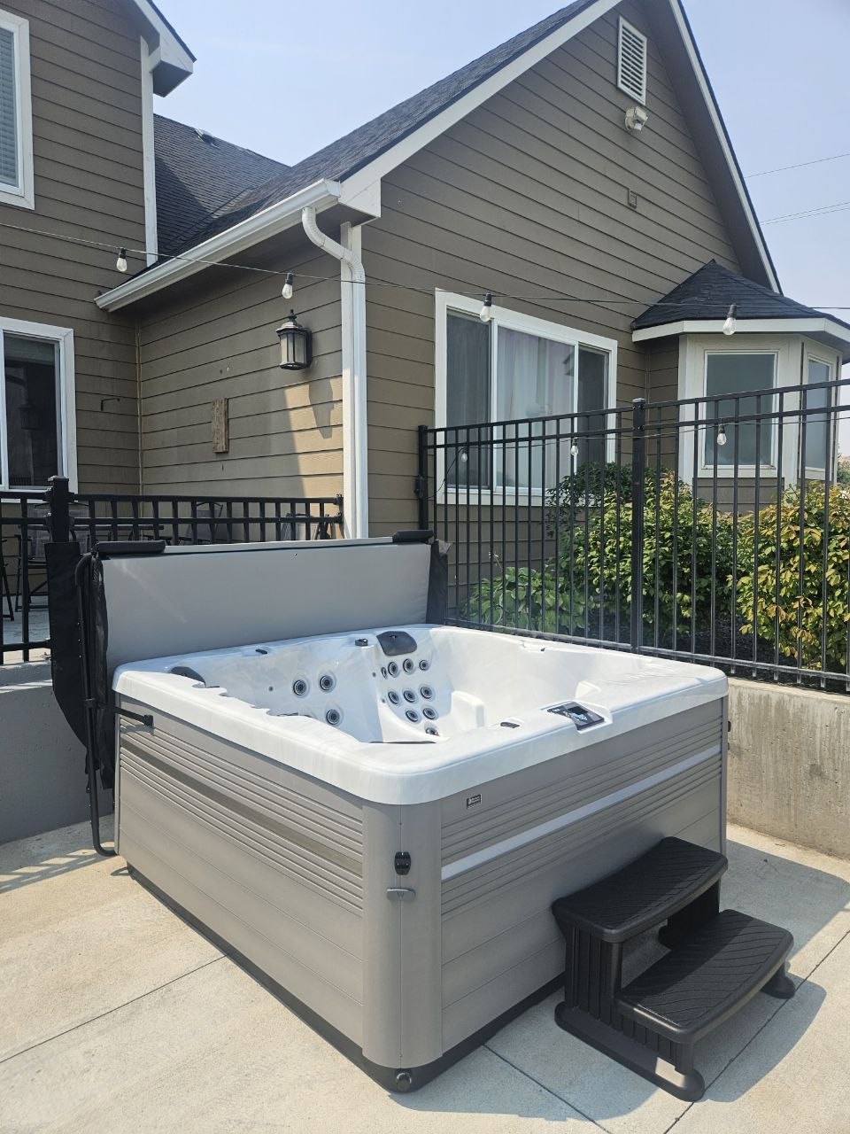 Vita Spa delivered on concrete patio with black iron fence and string lights — AquaZen Tri-Cities WA