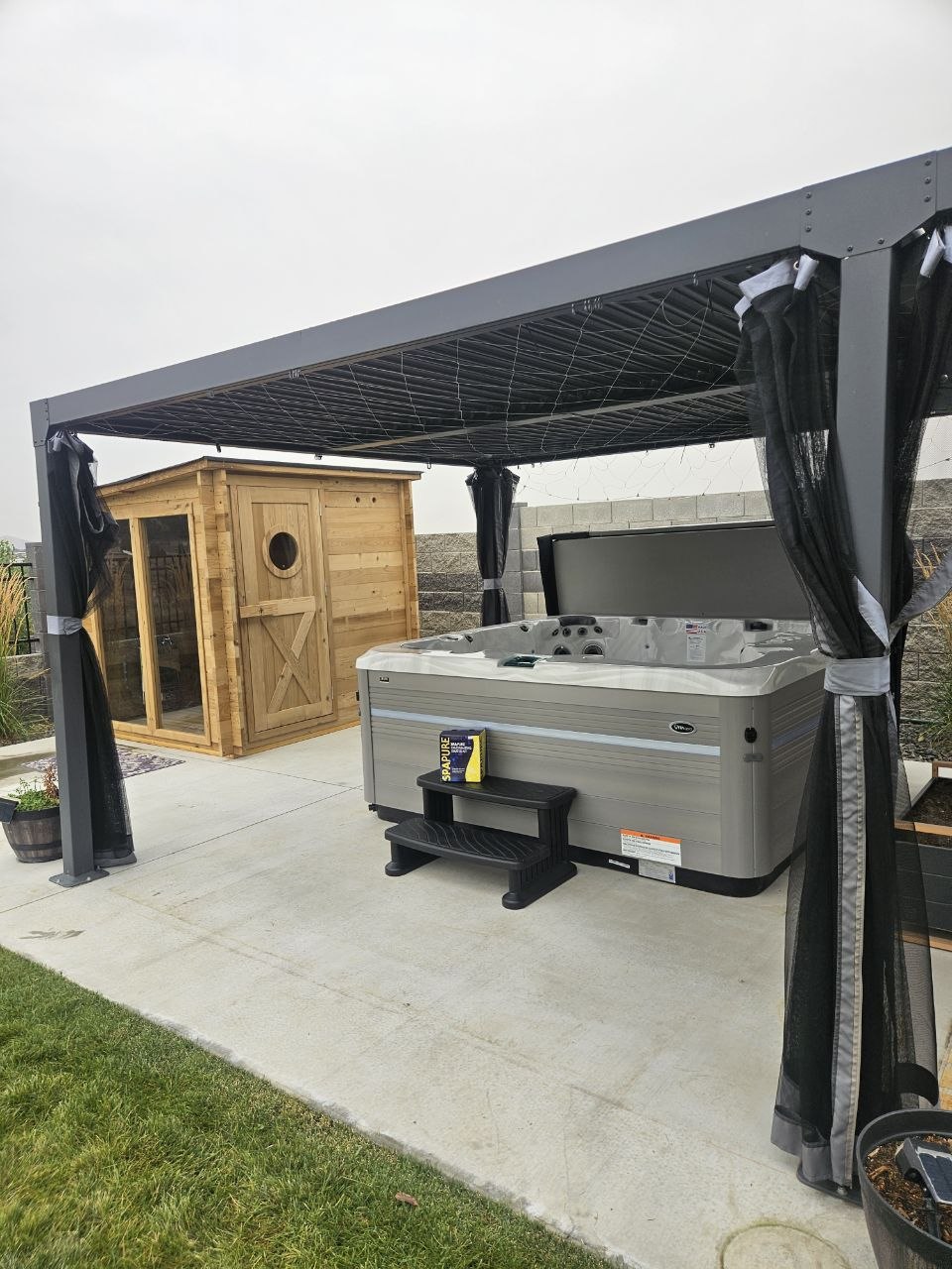 Vita Spa hot tub under black modern pergola with cedar sauna in background — delivered by AquaZen Richland WA